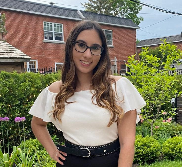 Robin Petrogiannis outdoors in a garden, standing in front of a red brick house.