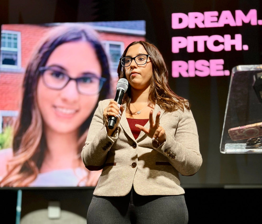 Robin Petrogiannis prend la parole sur scène, microphone en main, lors d'un événement de présentation, à côté d'un écran affichant son portrait et les mots "Dream. Pitch. Rise.".
