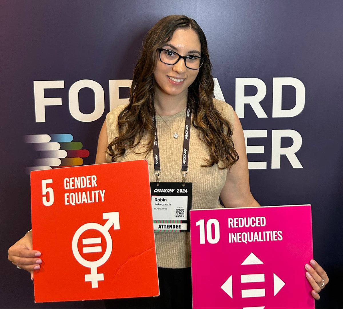 Robin Petrogiannis à Collision 2024, portant un cordon de participant et tenant deux pancartes des Objectifs de développement durable des Nations Unies : 5, Égalité entre les sexes, et 10, Inégalités réduites.